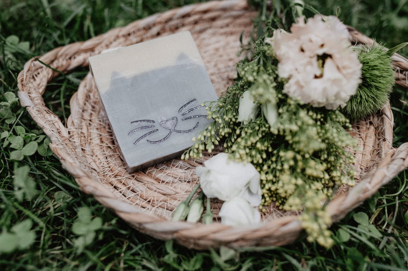 Handgemachte Seife mit Katzenmotiv in einem Korb mit Sommerblüten