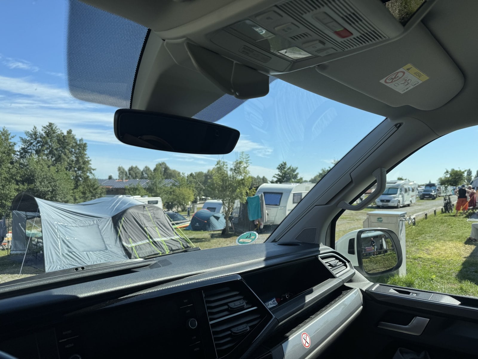 Blick aus dem gemieteten VW-Bulli auf einen Campingplatz mit Zelten und Wohnwagen – Wohnmobil mieten statt kaufen