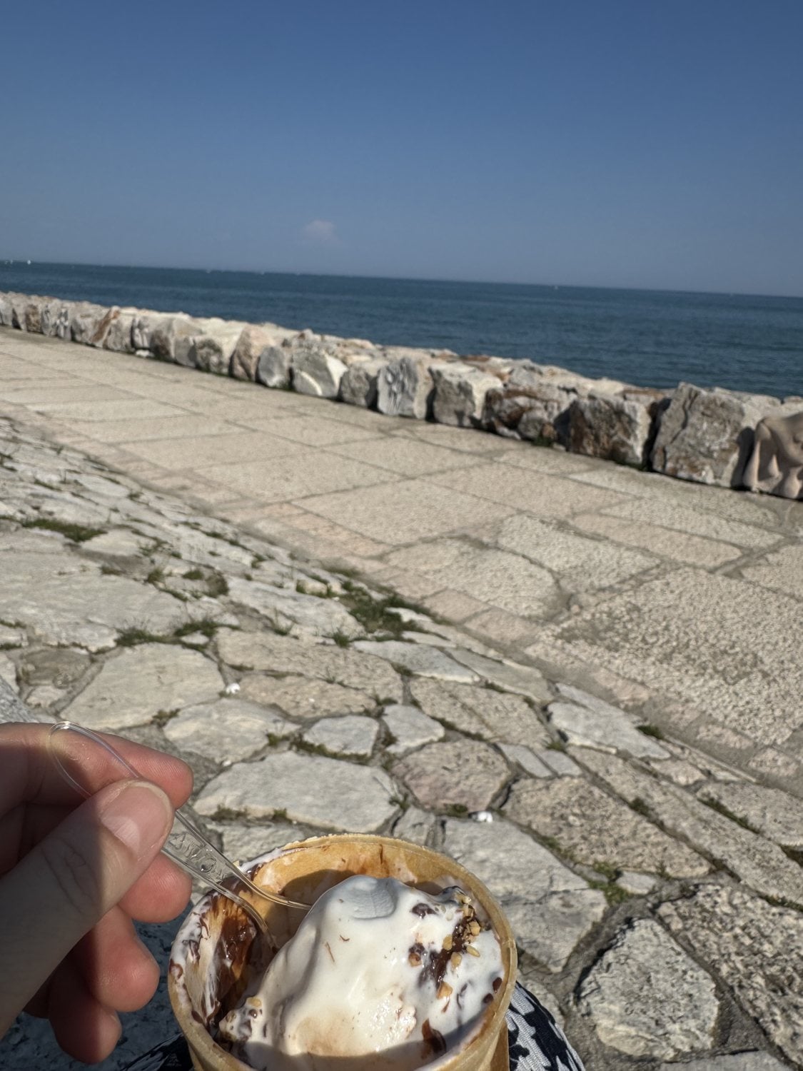 Becher Eis mit Sahne in der Hand auf der Strandpromenade am Meer in Caorle