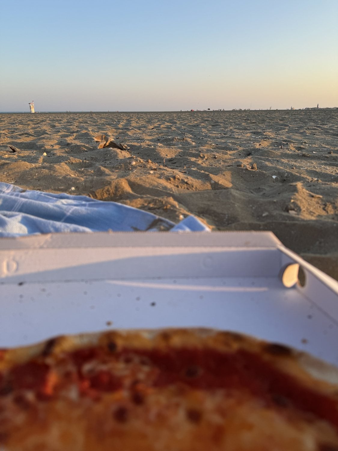 Pizzakarton am Sandstrand bei Sonnenuntergang am Meer in Italien