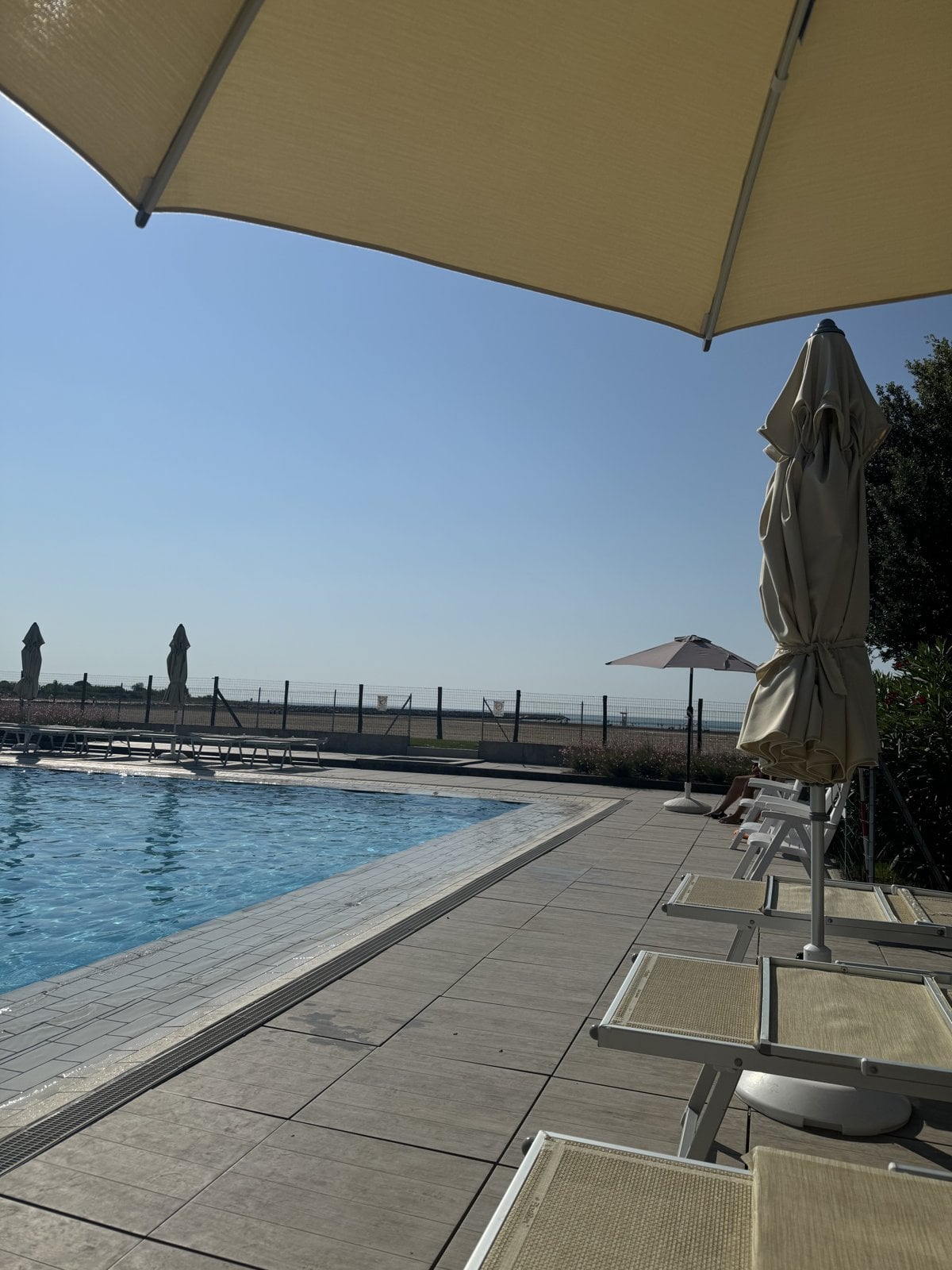 Menschenleerer Pool mit Sonnenschirmen und Liegen am frühen Morgen im Sommerurlaub in Italien