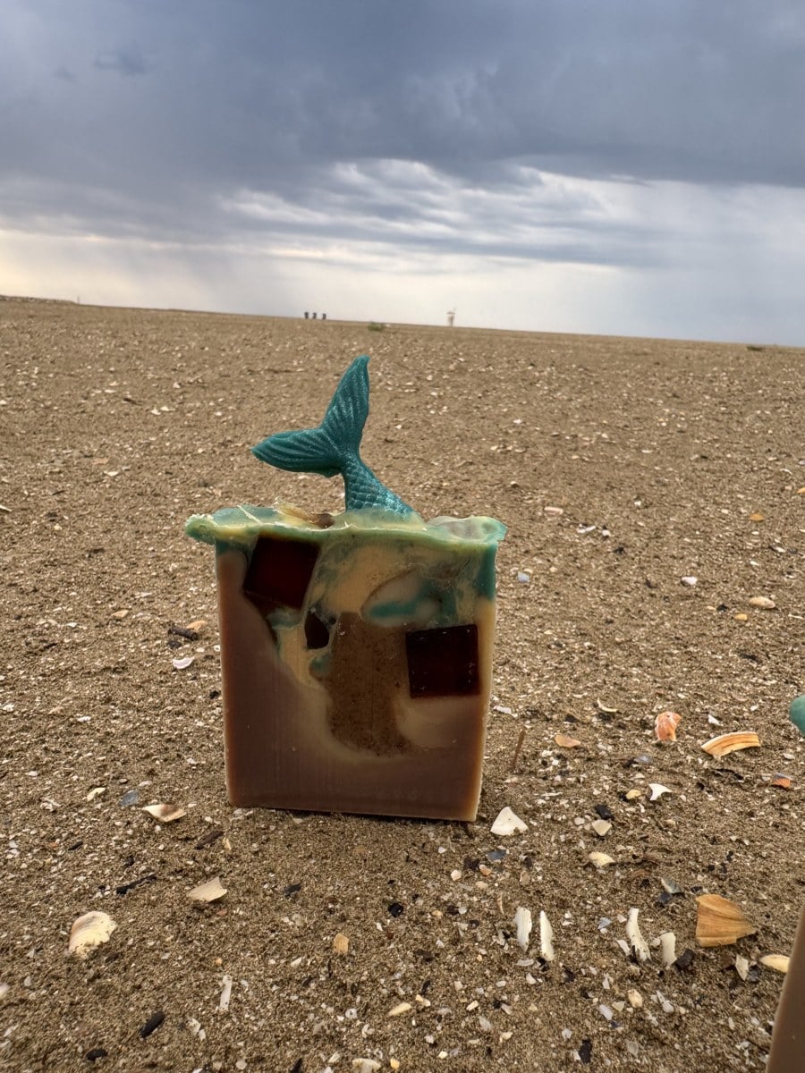 Handgesiedete Meerjungfrauen-Seife im Sand am Strand von Caorle, Meer im Hintergrund – Seife fotografieren im Urlaub